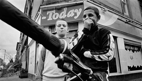 Two young men posing outdoors in front of a storefront with "Today" signage visible above them.