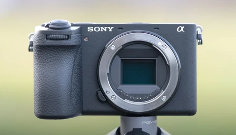 Sony Alpha mirrorless camera body with open lens mount displayed against a blurred yellow-green background.