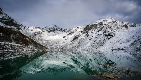 Snow-covered mountain slopes surrounding a turquoise alpine lake under overcast sky.