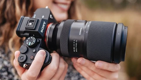 Photographer holding a Sony mirrorless camera with a telephoto lens and external flash mounted on top.