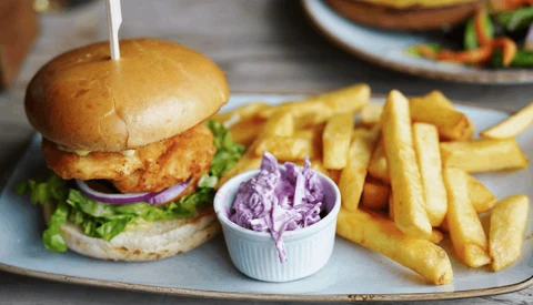 Crispy fried chicken sandwich with lettuce and purple onion on a bun, served with golden fries and purple cabbage slaw.