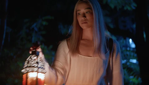 Woman holding illuminated lantern outdoors at night with cool blue ambient lighting.