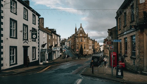 Scottish street lined with historic stone buildings and a red telephone box, sloping downward toward a church spire in the distance.
