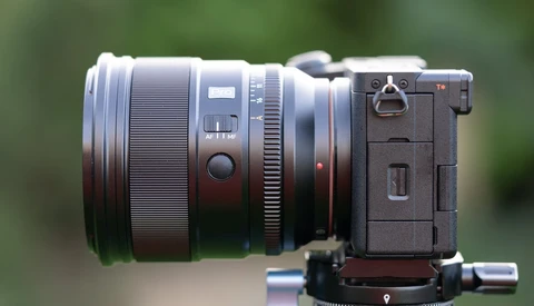 Mirrorless camera with large telephoto lens mounted on gimbal head, photographed against blurred green background.
