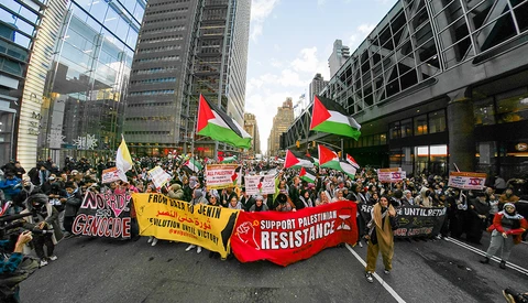 Large protest march filling a city street with Palestinian flags and demonstrators holding signs.
