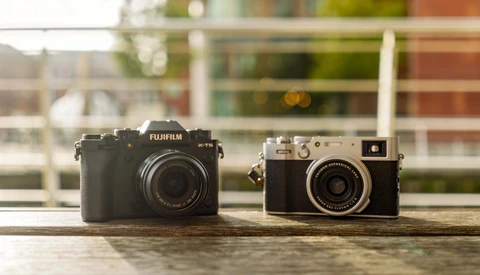 A modern Fujifilm mirrorless camera positioned next to a vintage rangefinder camera on a wooden surface.