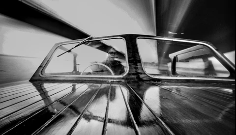 Black and white photo taken from inside a moving car, showing the windshield and interior with motion blur streaking across the frame.