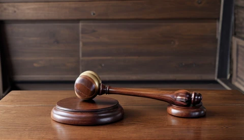 Wooden gavel and sound block arranged on a polished wood desk against a dark wooden background.