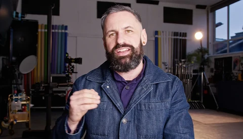 Bearded man in denim jacket smiling at camera in professional studio setting.