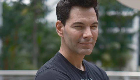 Man in dark t-shirt looking over shoulder toward camera with natural outdoor lighting.