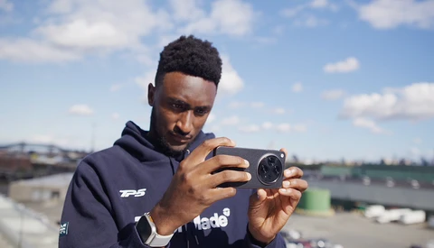 Photographer holding a compact camera while looking at the LCD screen in outdoor daylight.