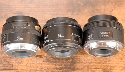 Three 50mm prime lenses arranged side by side on a wooden surface for comparison.