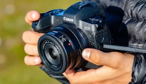 Photographer holding a Canon EOS camera with a prime lens in outdoor daylight.