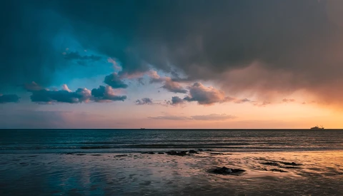 Dramatic sunset over a calm ocean with golden and blue-tinted clouds reflecting on the water.
