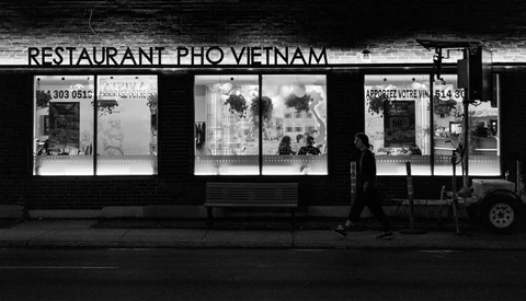 Black and white storefront of a Vietnamese pho restaurant with three large display windows and illuminated signage at night.
