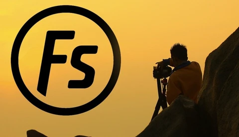 Silhouetted photographer operating a camera on a rocky outcrop against a golden yellow sky with the Fstoppers logo.