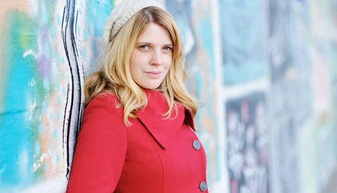 Woman in red jacket leaning against colorful graffiti wall, looking at camera.