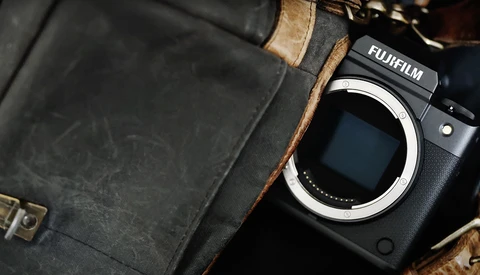 Fujifilm mirrorless camera body next to vintage leather camera bag with brass hardware.