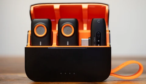 Portable wireless microphone system with charging case displaying two black microphones with orange accents and a receiver unit.