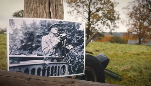 Black and white photograph mounted on tree trunk, showing person in vintage military vehicle, overlaid on autumn landscape.