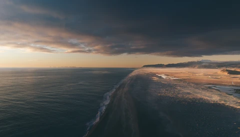 Aerial view of a sandy coastal spit extending into dark ocean waters at dusk.