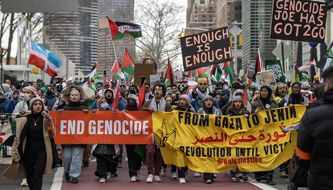 Large crowd of protesters holding banners and flags during an outdoor march in an urban setting.