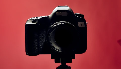 Canon DSLR camera with telephoto lens mounted on tripod against red backdrop.