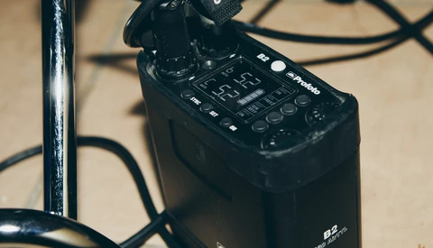 Black audio recorder with control panel and microphone attachment on beige surface with cables.