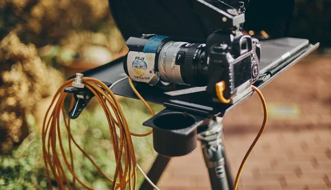 Film camera mounted on a rig with coiled orange cables and external audio equipment attached.