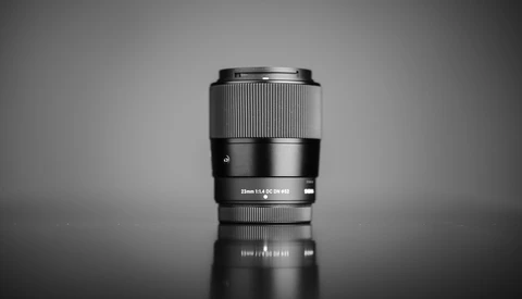 Sony mirrorless camera lens with silver and black barrel standing upright against neutral background.