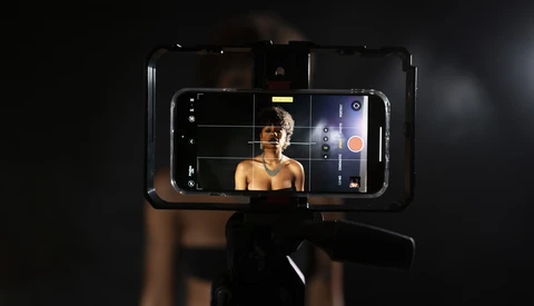 Smartphone mounted on a gimbal displaying a portrait of a shirtless man in a dark studio setting.