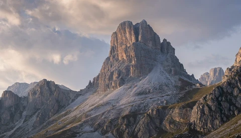 Dramatic alpine peak with steep columnar rock formations and early snow in golden hour light.