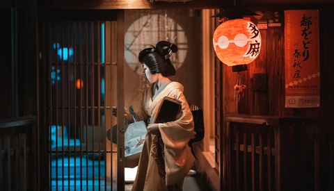 Woman in traditional kimono and geisha makeup standing in a narrow alley lit by blue neon and warm lantern light.