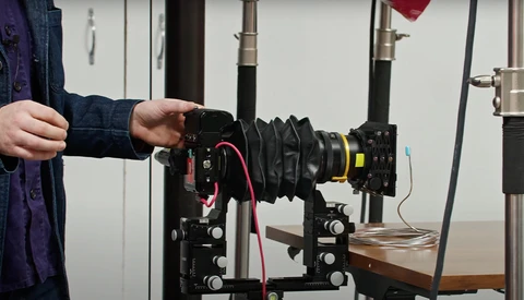 Photographer adjusting a lens on a cinema camera mounted to a wooden support rail.