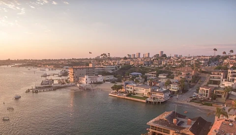 Coastal waterfront neighborhood at golden hour with bay, docks, and distant skyline under clear sky.