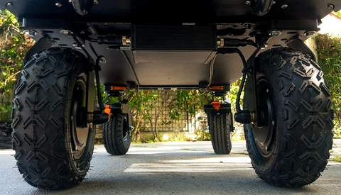 Undercarriage view of an all-terrain vehicle with large knobby black tires and yellow suspension components.