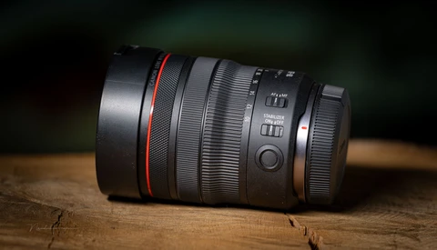 Telephoto zoom lens with red accent ring positioned on wooden surface against dark background.