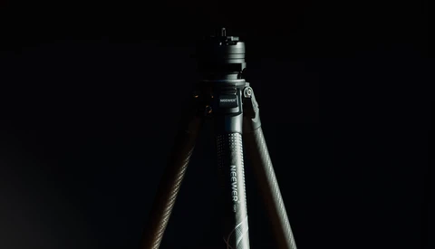 Tripod head mounted on pole against dark background with dramatic sidelighting.