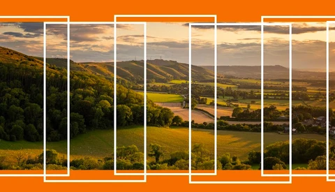 Rolling countryside landscape with agricultural fields and forested hills under golden hour sky.