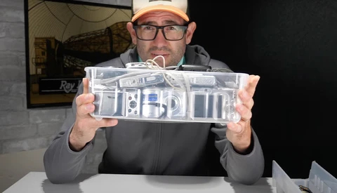 Person holding a clear acrylic case containing camera parts and accessories during a product demonstration.