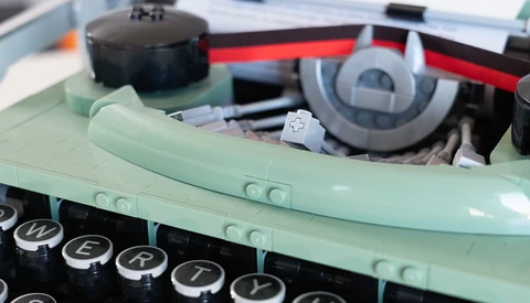 Close-up of a vintage typewriter with mint green body and black keys, showing mechanical components and ribbon mechanism inside.