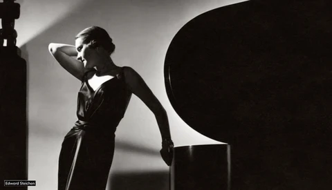 Woman in dark dress poses against geometric black shapes in high-contrast studio lighting.