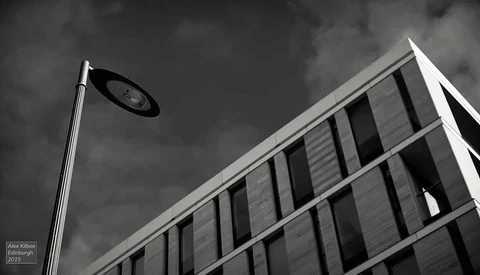 Street lamp against dramatic cloudy sky with modernist building facade featuring vertical window lines.