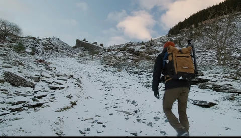 Backpacker hiking across snowy alpine terrain with yellow and brown pack on their back.