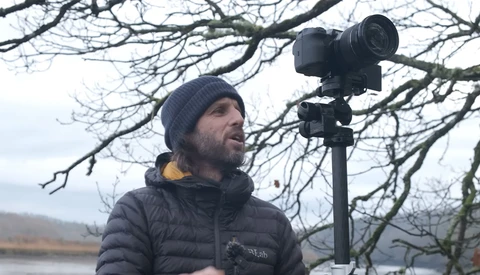 Videographer in winter gear operating a professional mirrorless camera on a tripod overlooking a winter landscape.