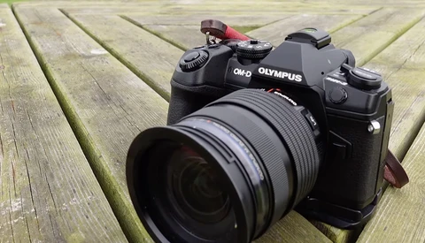 Olympus OM-D mirrorless camera with attached zoom lens on wooden deck surface.
