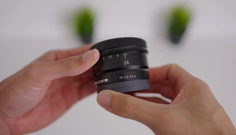 Hands holding a wide-angle camera lens with manual focus ring and aperture markings visible.
