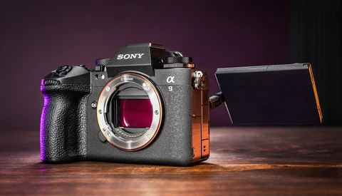 Sony α8 mirrorless camera body with open articulating screen, lit with purple and orange accent lighting against dark background.