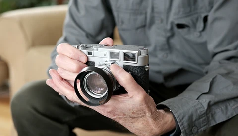 Hands holding a vintage rangefinder camera with a wide-angle lens attached.