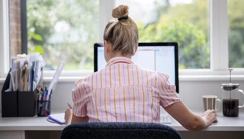 Person working at desk with laptop, viewed from behind, natural window light streaming across workspace.